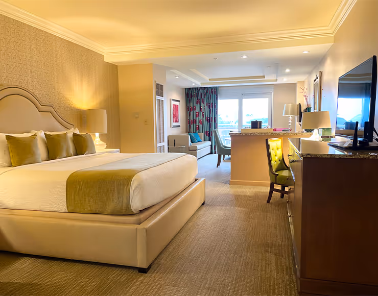 A spacious and well-appointed hotel room with a large bed, plush furnishings, and a seating area visible in the background.