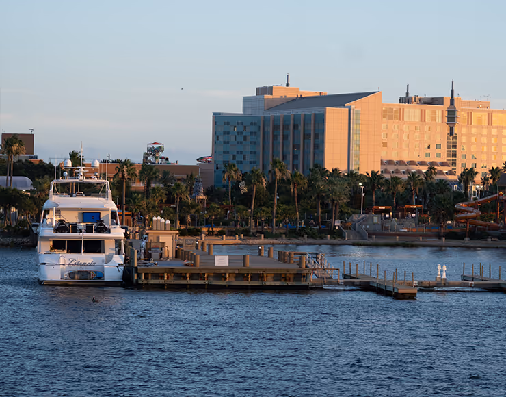 A waterfront scene with a boat docked in the foreground and tall buildings, including a hotel, in the background against a clear sky.