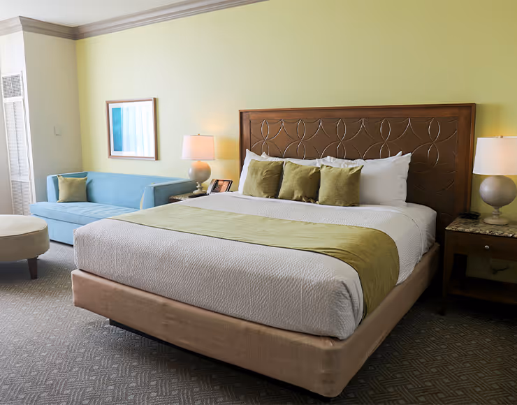 A cozy and inviting bedroom with a large bed, plush bedding, and a wooden headboard. The room features a blue sofa and framed artwork on the walls, creating a warm and comfortable atmosphere.