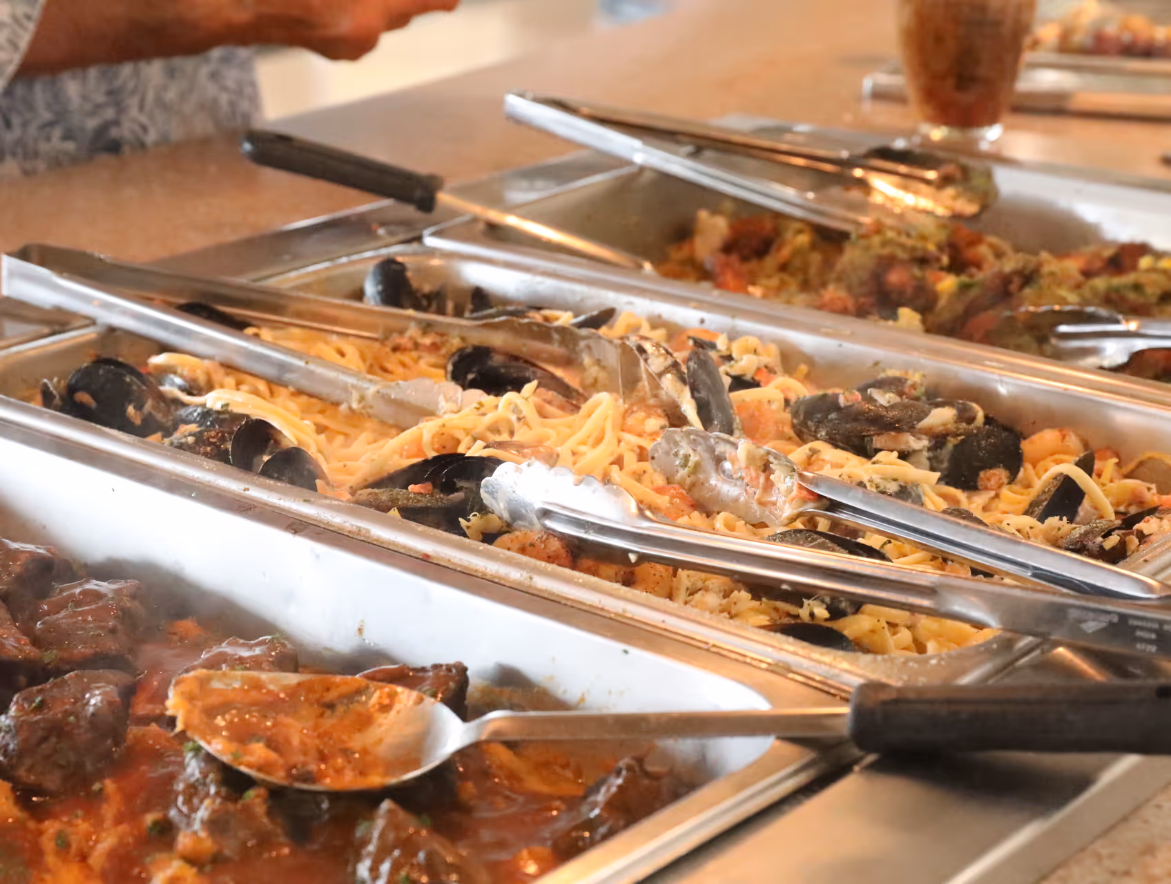 Family of three sits on a bed while the mom points to something in a book that a child is reading.