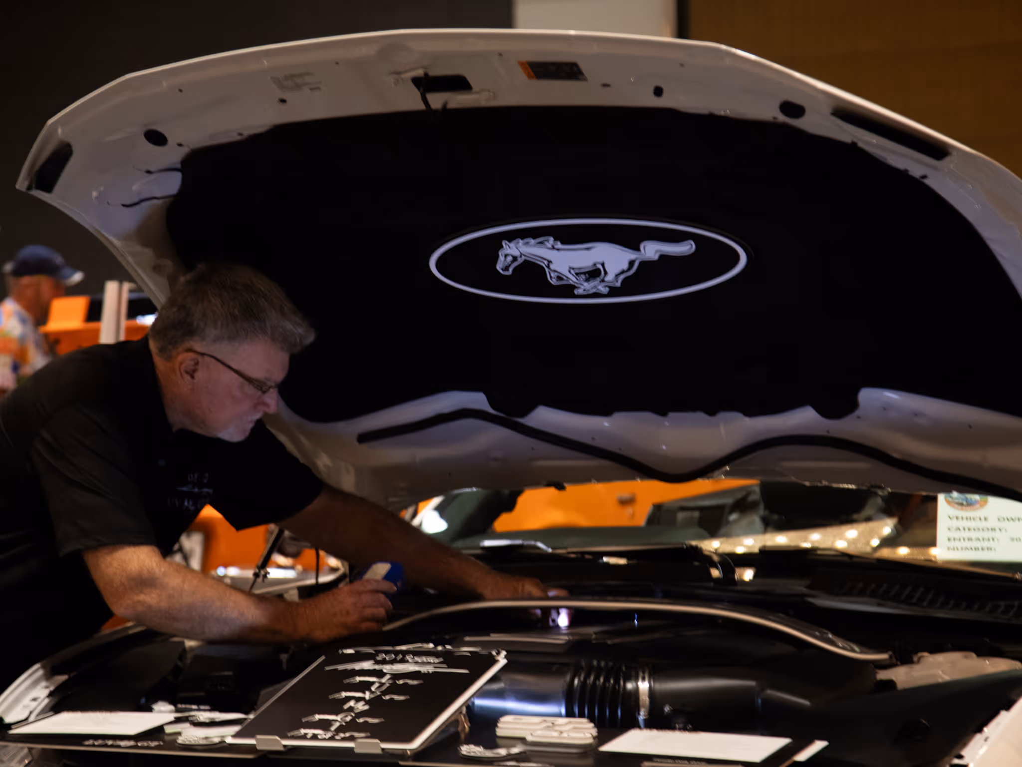 A visitor looks under the open hood of a white Ford Mustang at the Moody Gardens Car Show