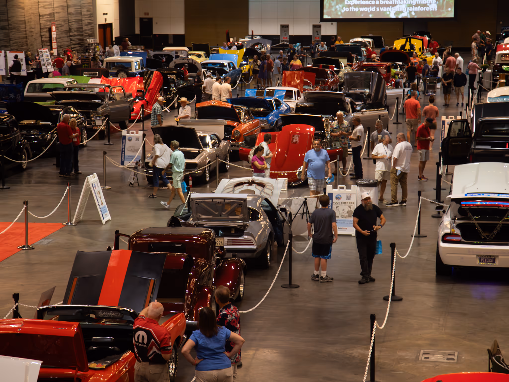 Rows of classic and modern cars with visitors walking the floor at the Moody Gardens Car Show in the Convention Center