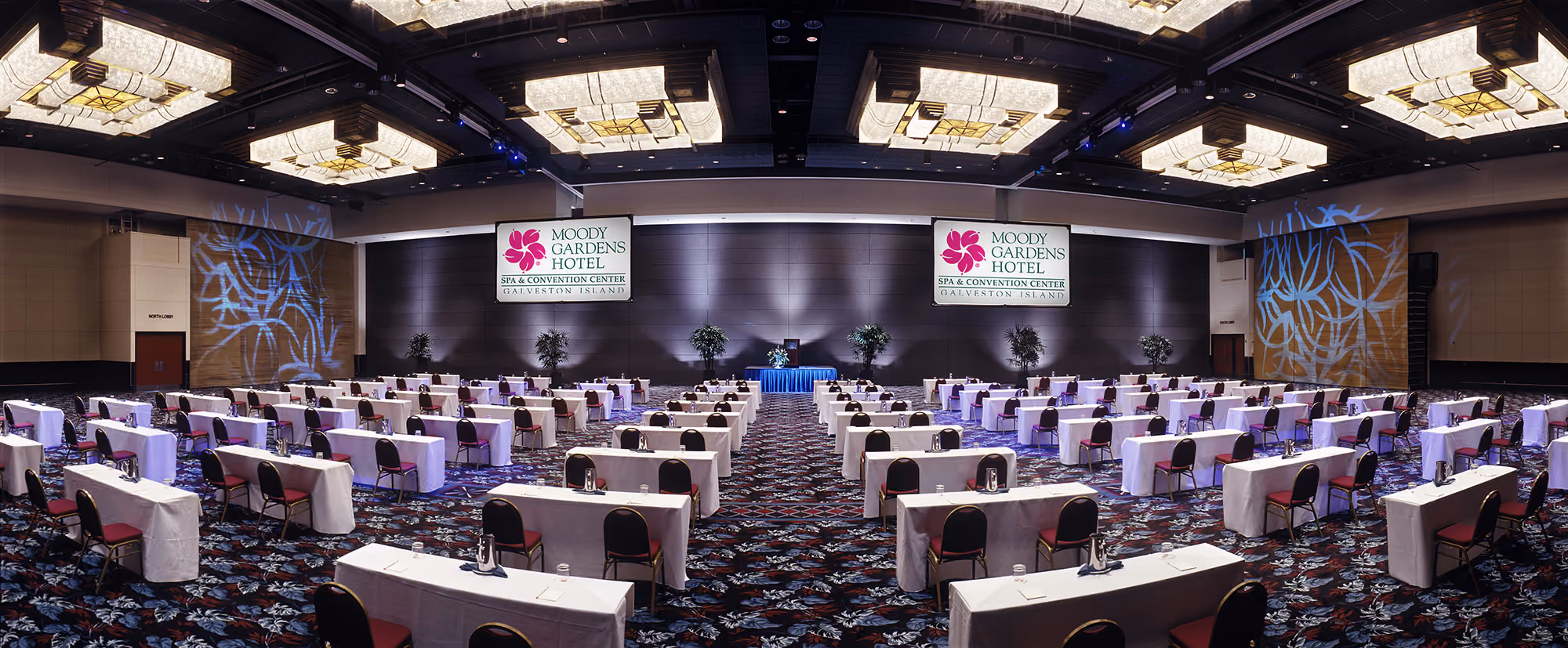 Two individuals, a woman and a man sitting in the executive conference room located on the 9th floor of the Moody Gardens hotel for a meeting. The woman is showing the man an item on her laptop display screen as he looks up from behind his own laptop. 