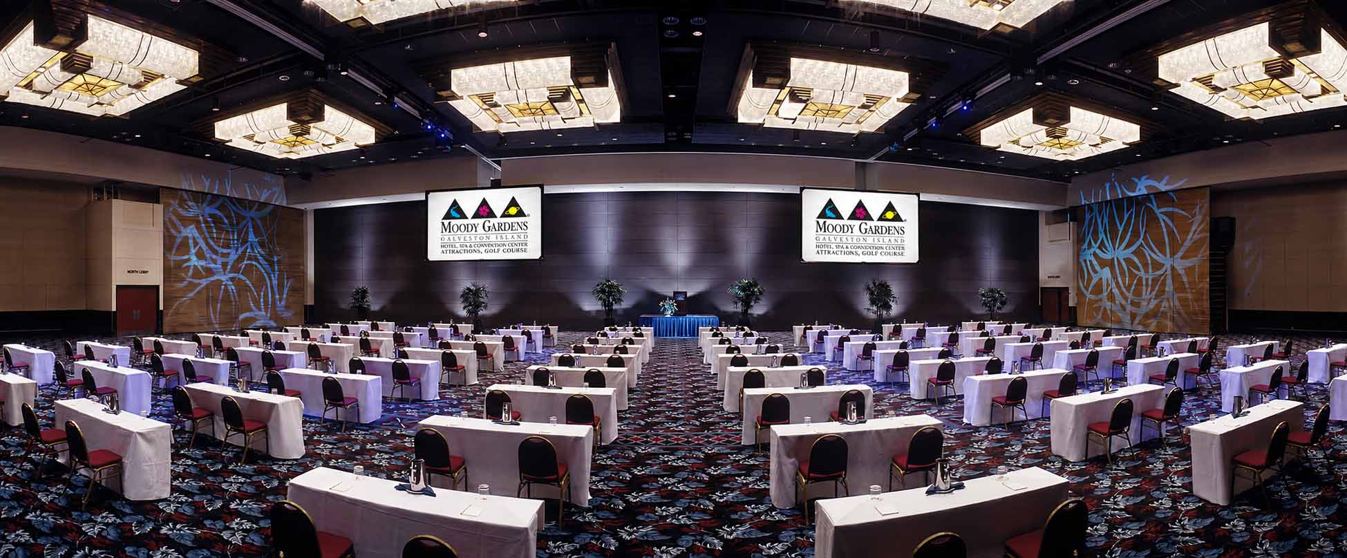 Two individuals, a woman and a man sitting in the executive conference room located on the 9th floor of the Moody Gardens hotel for a meeting. The woman is showing the man an item on her laptop display screen as he looks up from behind his own laptop. 