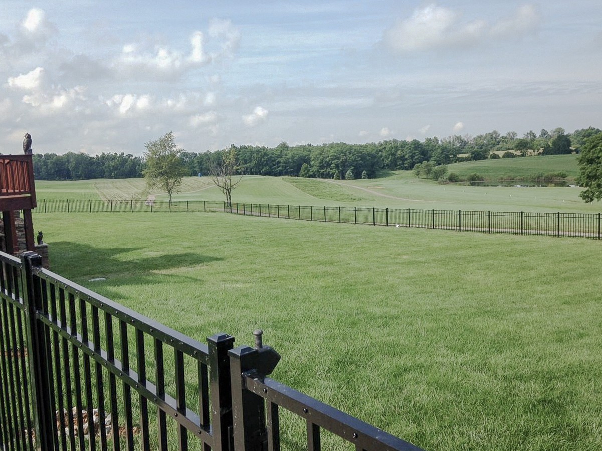 Aluminum gate in the foreground with an open lawn and fence beyond.