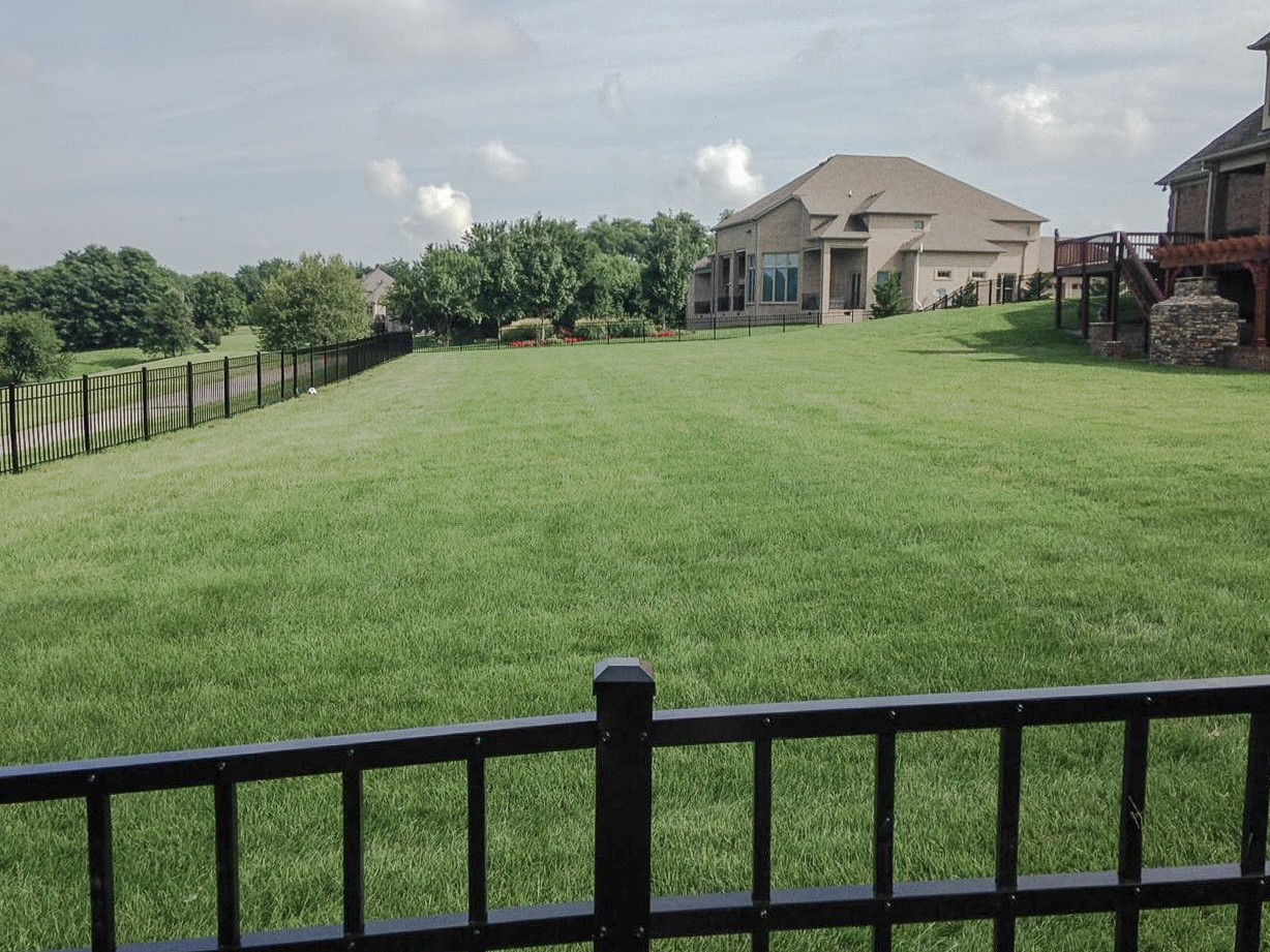 Fenced lawn extending uphill toward a brick home and raised deck.