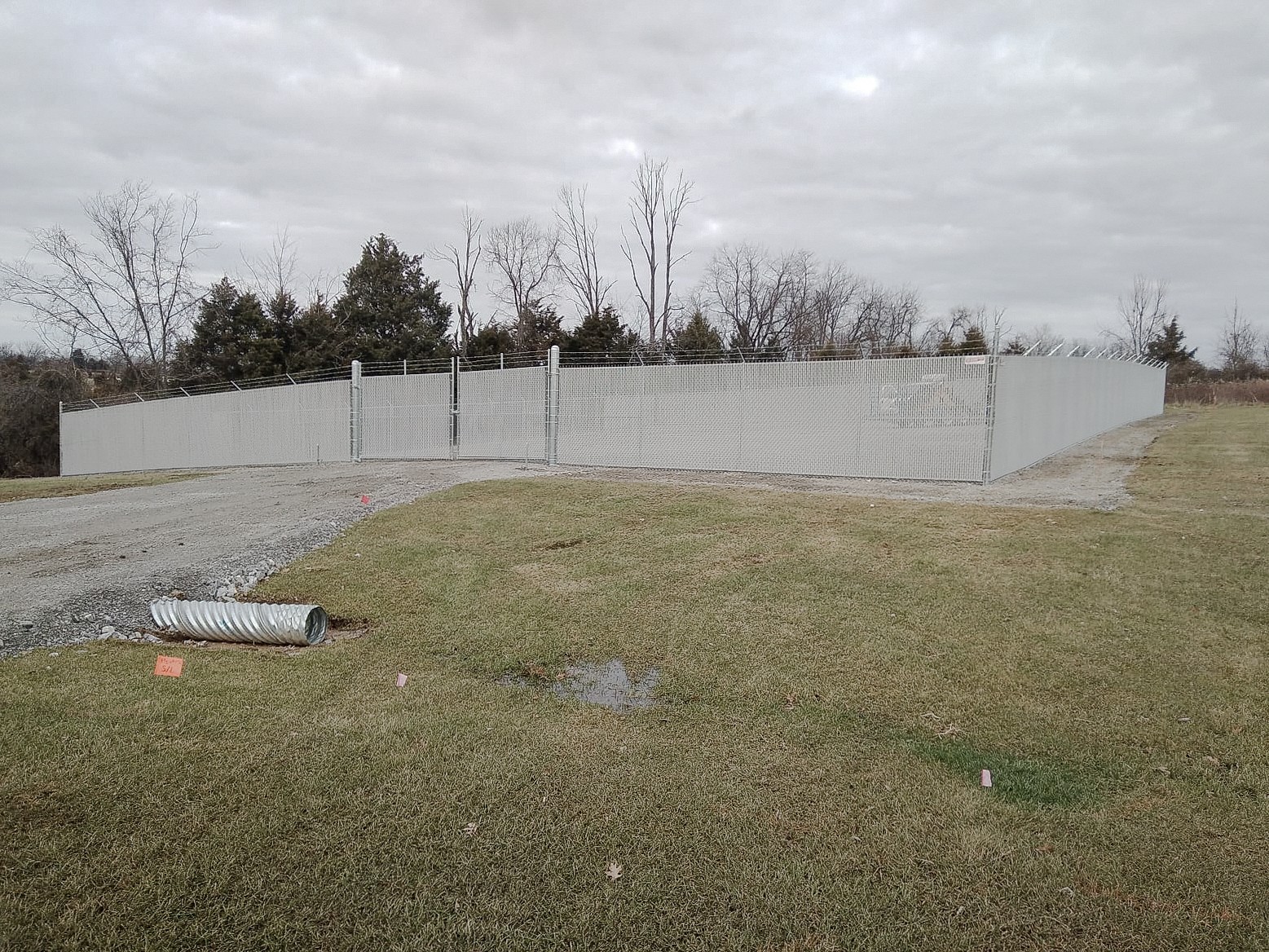 Privacy-slat fence turning a corner beside grass and a gravel entrance.