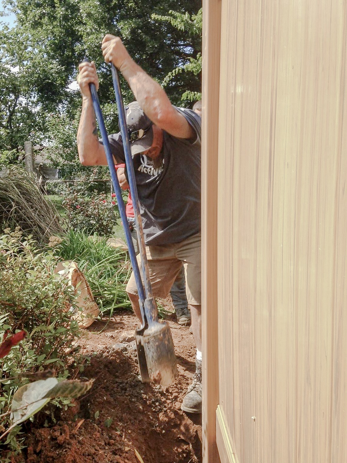 Installer using a post-hole tool beside a vinyl privacy panel.