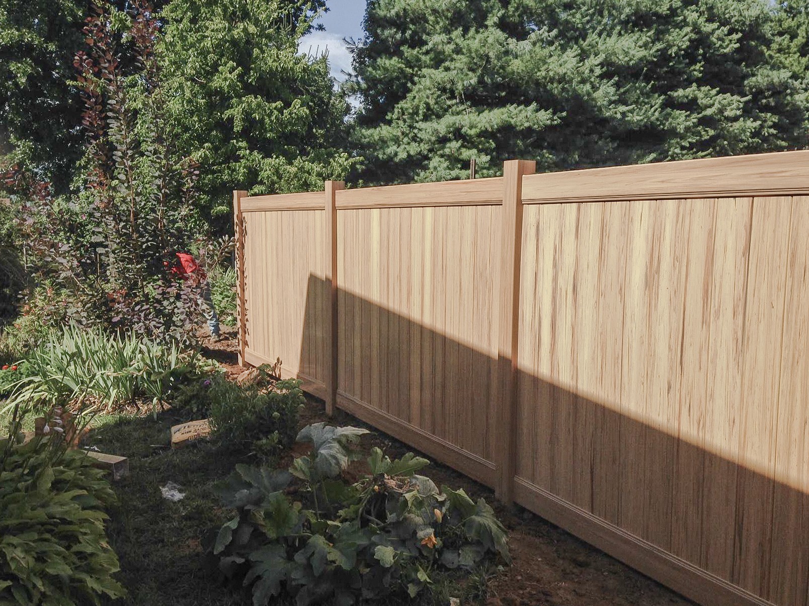 Vinyl privacy panels beside a planted garden bed with sunlight and shade.