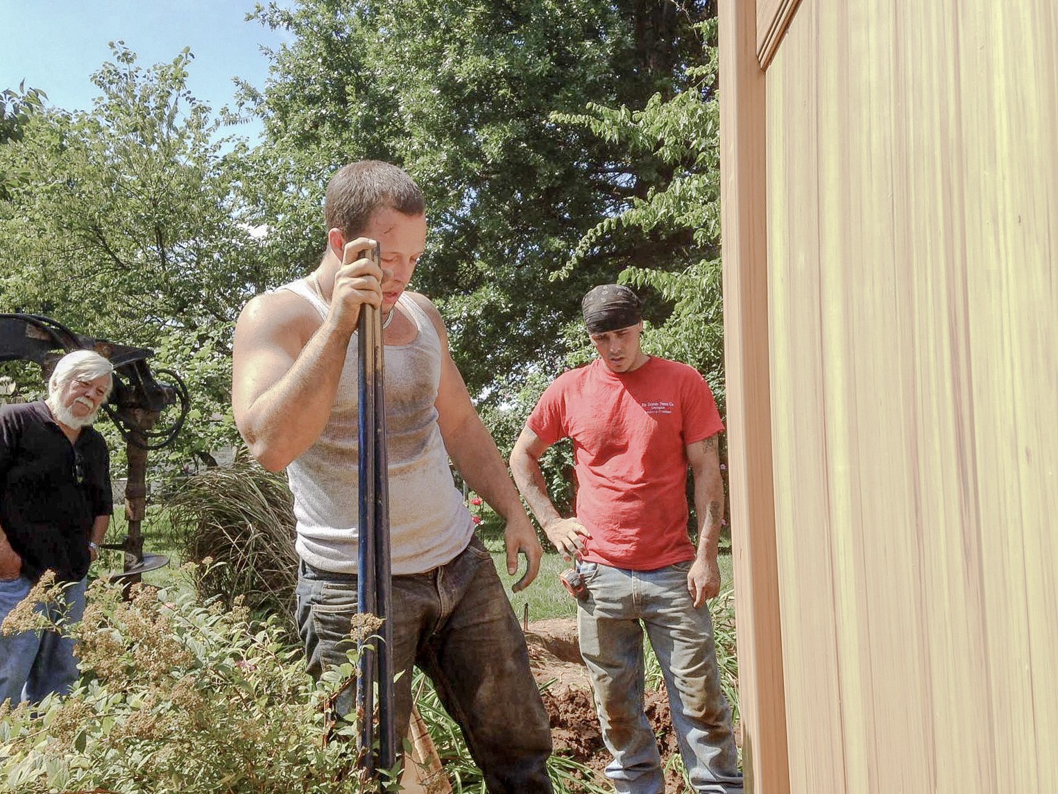 Crew working on a vinyl fence post beside a garden bed.