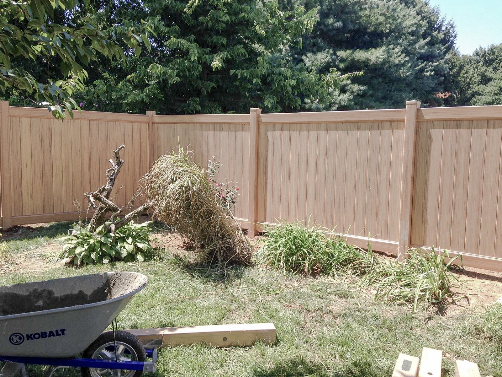 Vinyl privacy fence meeting at a garden corner with a wheelbarrow in front.