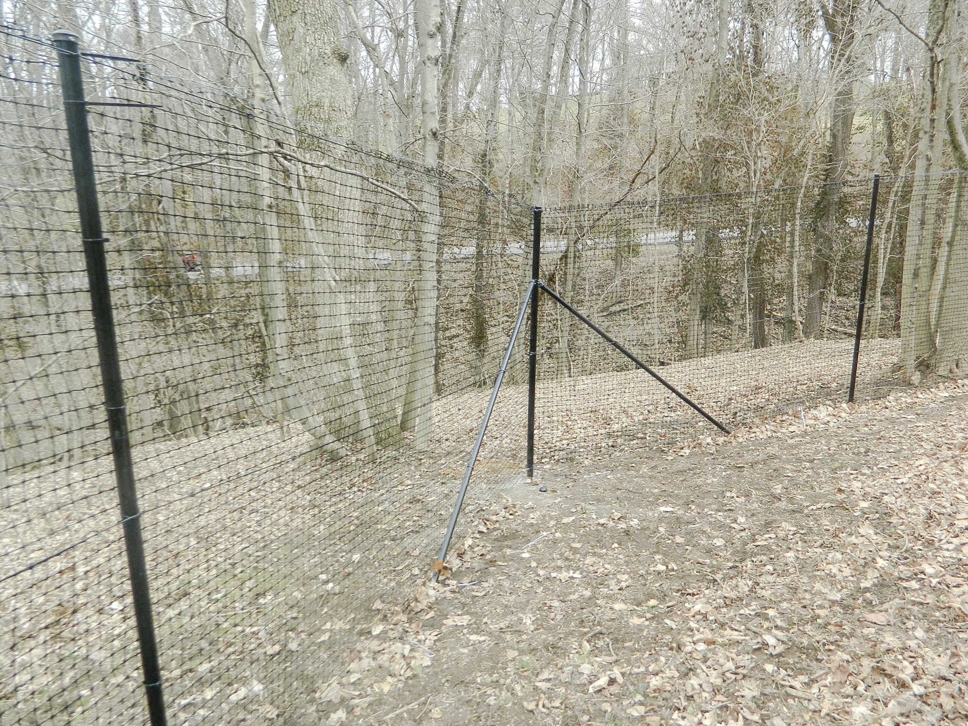 Braced fence post beside a mesh perimeter on a wooded slope.