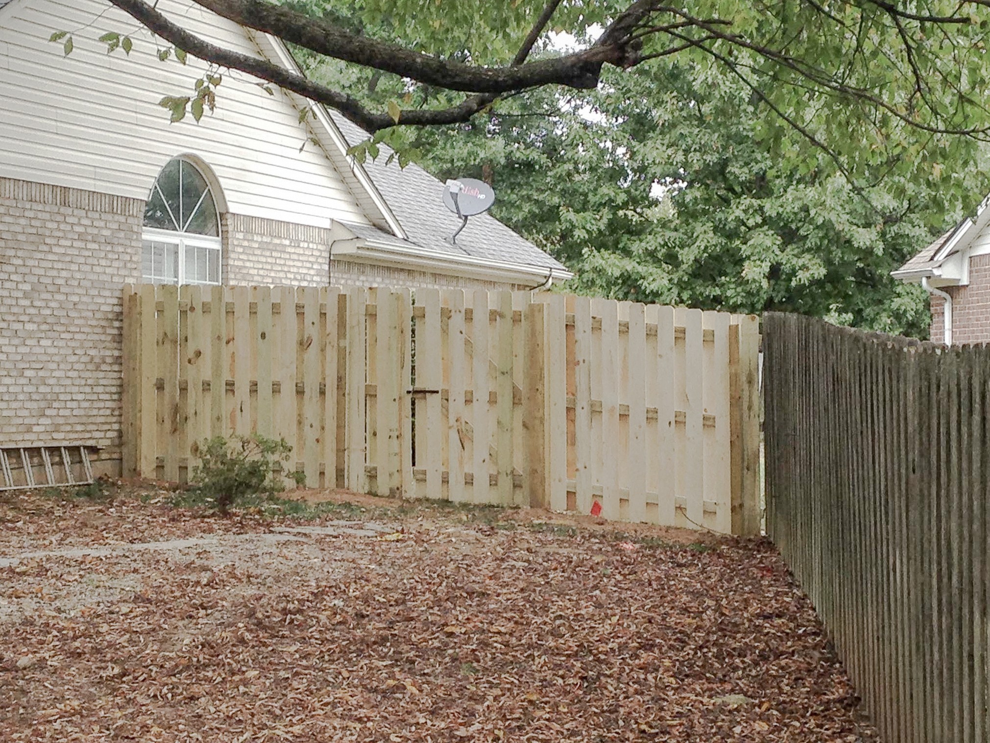 Wood fence and double-gate area beside a home beneath a large tree branch.