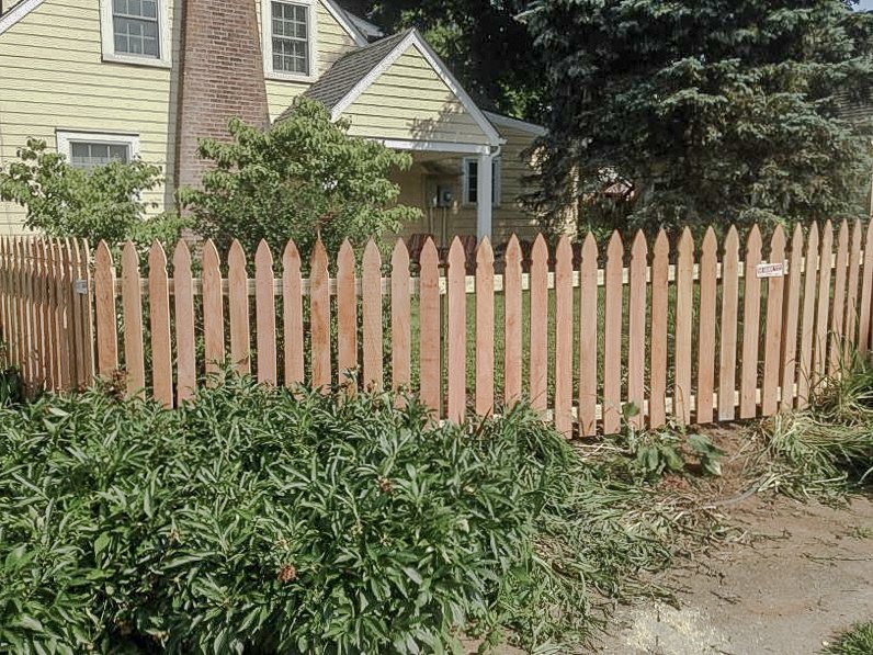 Gothic-top cedar pickets following a curved garden edge beside the house.