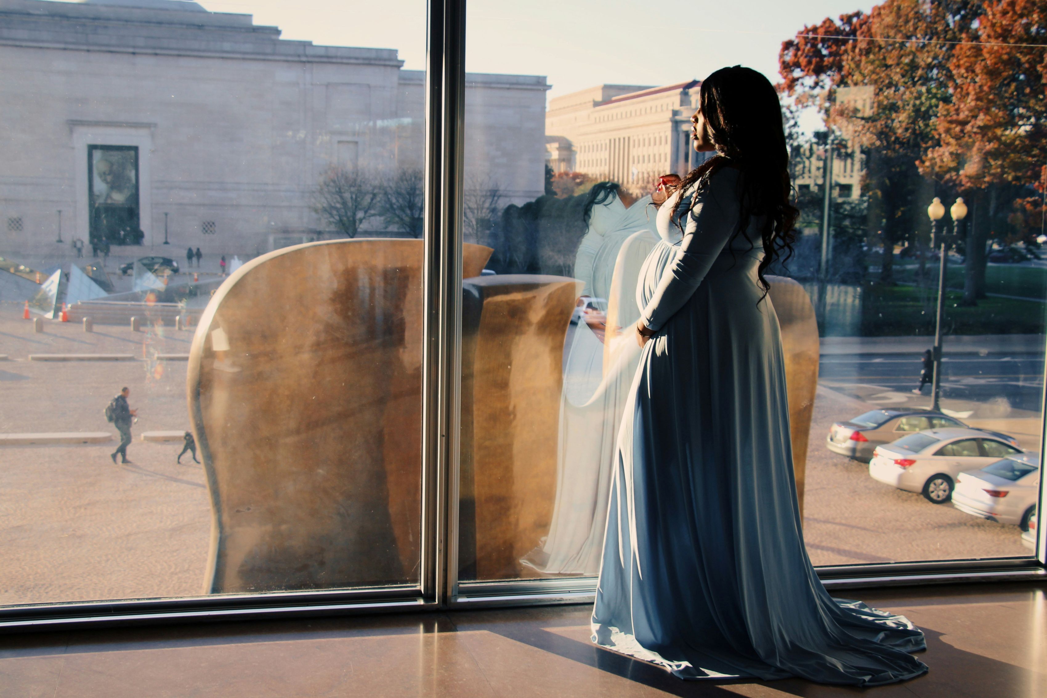 pregnant woman holding belly and looking out window onto street