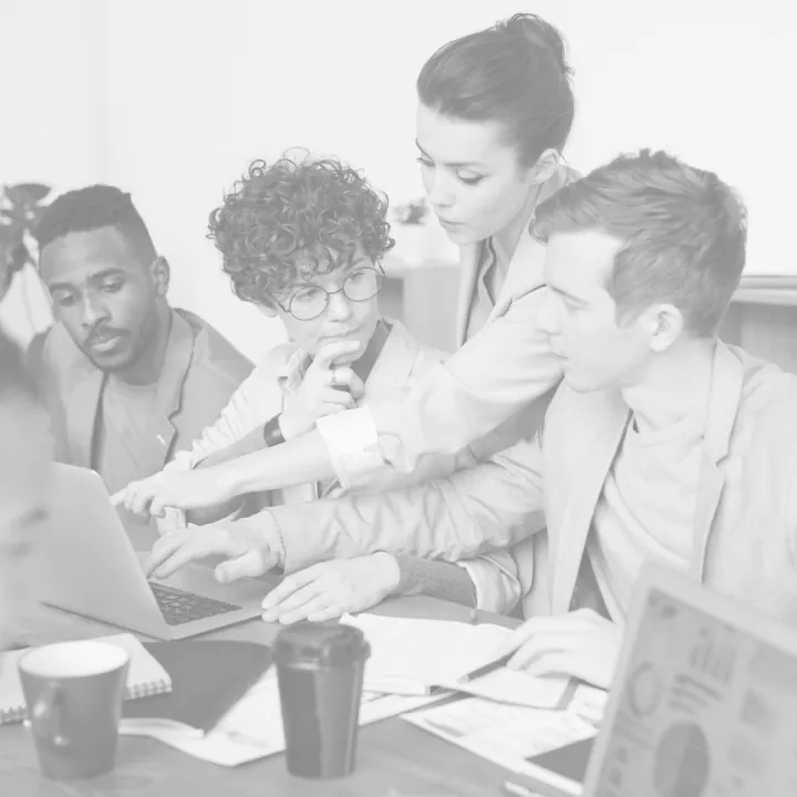 A group of people sitting around a table working on a laptop.