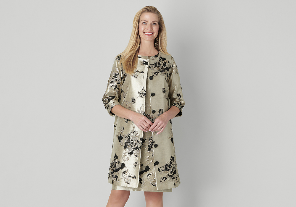 Model wearing a metallic gold coat with black floral embroidery and three-quarter sleeves, paired with a matching skirt from the Caroline Rose Fall 2025 collection.