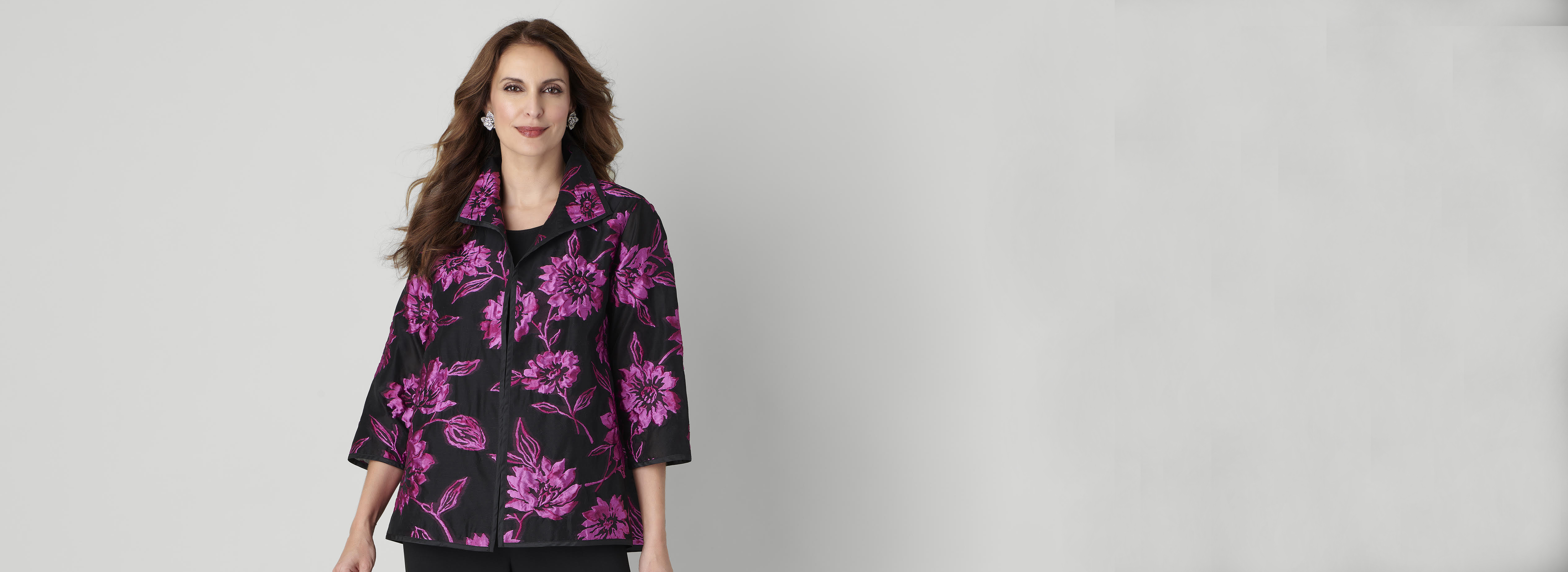 A woman standing in front of a white wall with a black jacket and pink floral print
