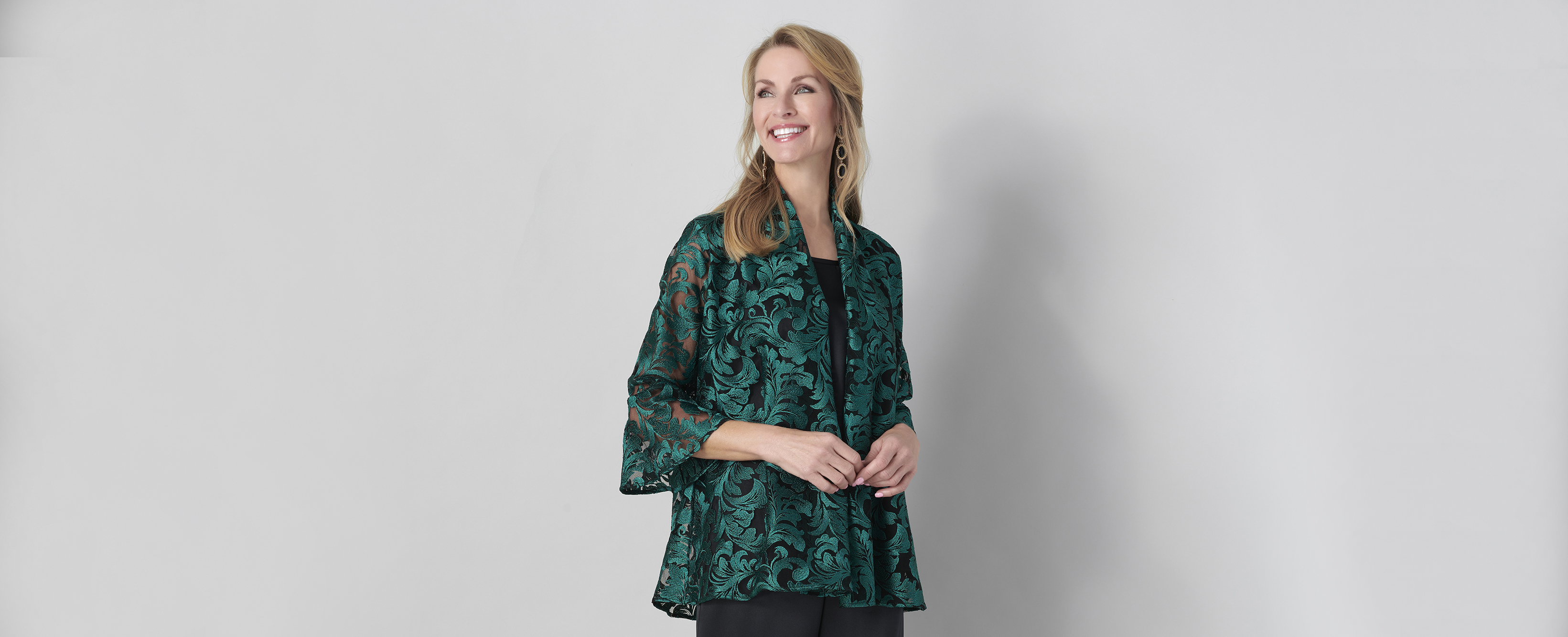 A woman standing in front of a white wall wearing a green and black jacket and pants