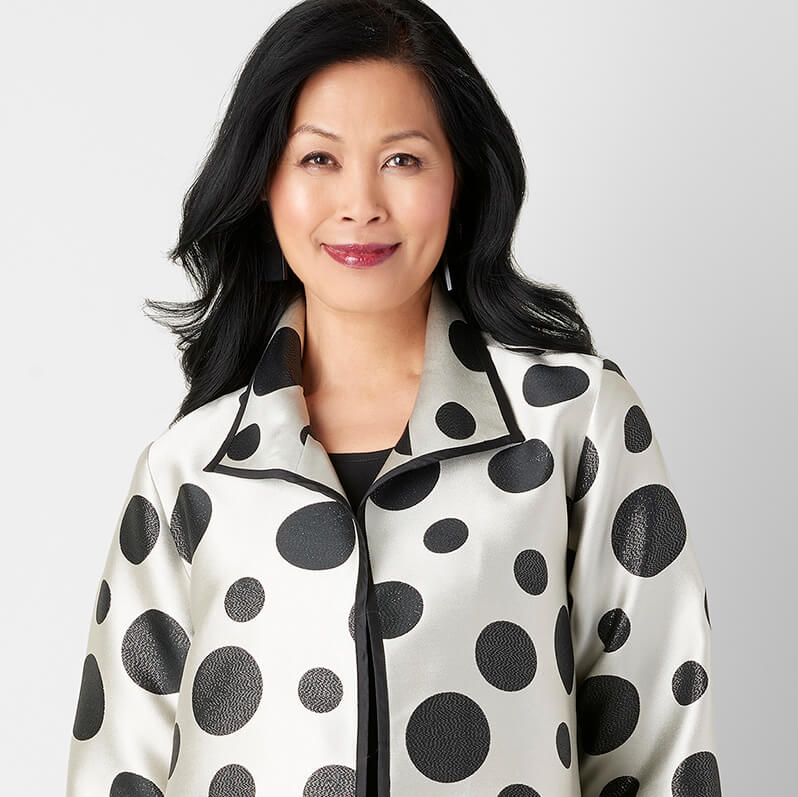 Smiling woman wearing a white jacket with large black polka dots and black trim.