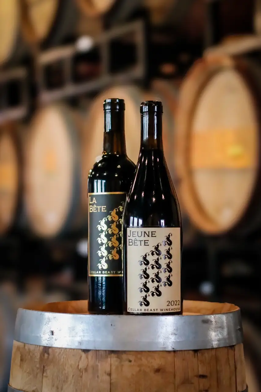 Two Cellar Beast Winehouse bottles — 2024 Jeune Bête and 2022 La Bête — resting on French oak barrels inside Cellar Beast Winehouse.