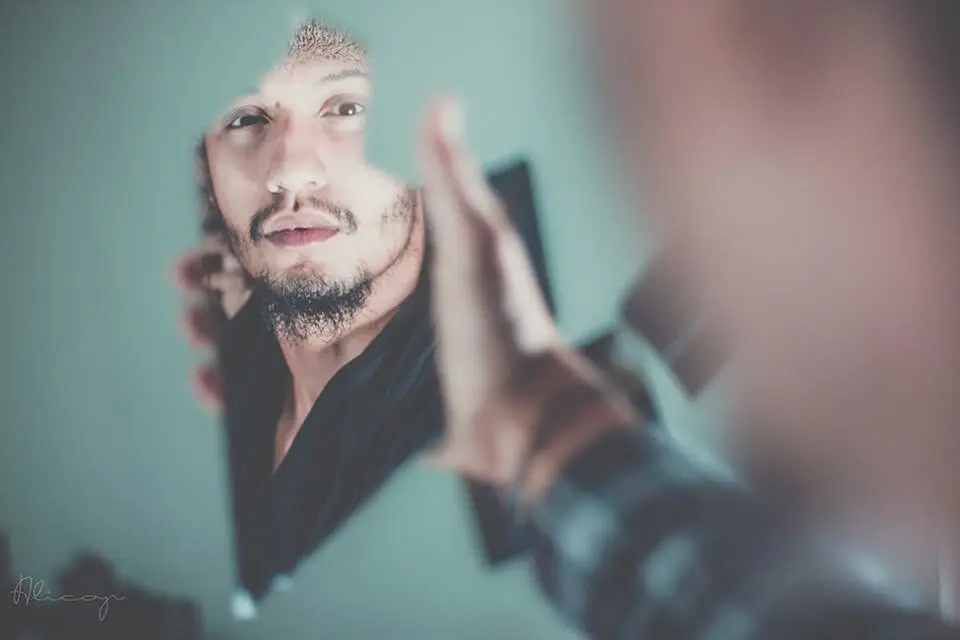 Man looking at a reflection of himself in a broken shard of a mirror