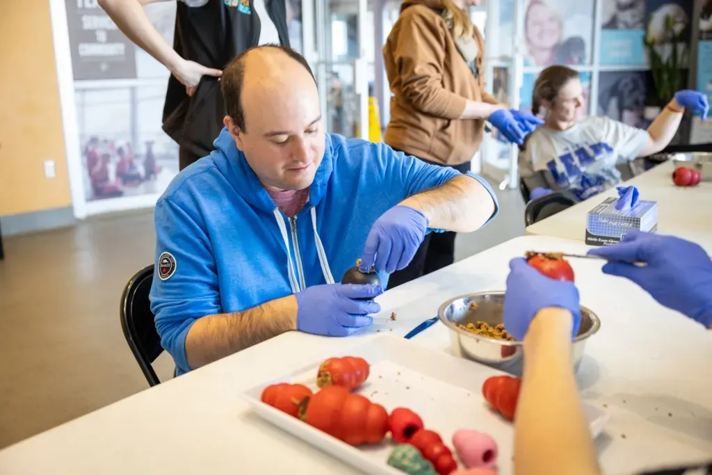 People wearing blue gloves sit around a table engaging in a hands-on activity with red and black round objects.