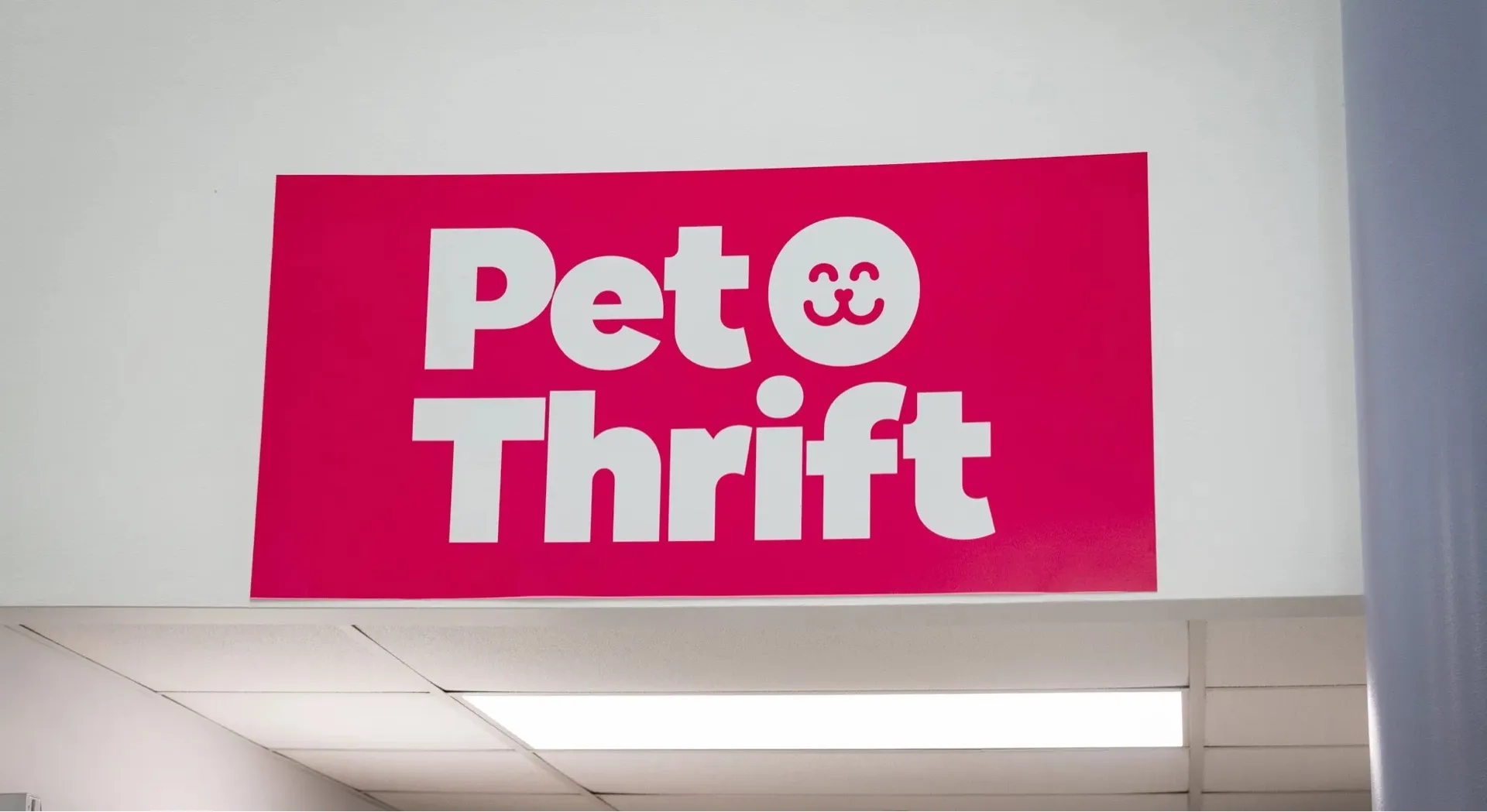 Bright pink sign with bold white text reading 'Pet Thrift' and a smiling cat face emoji.