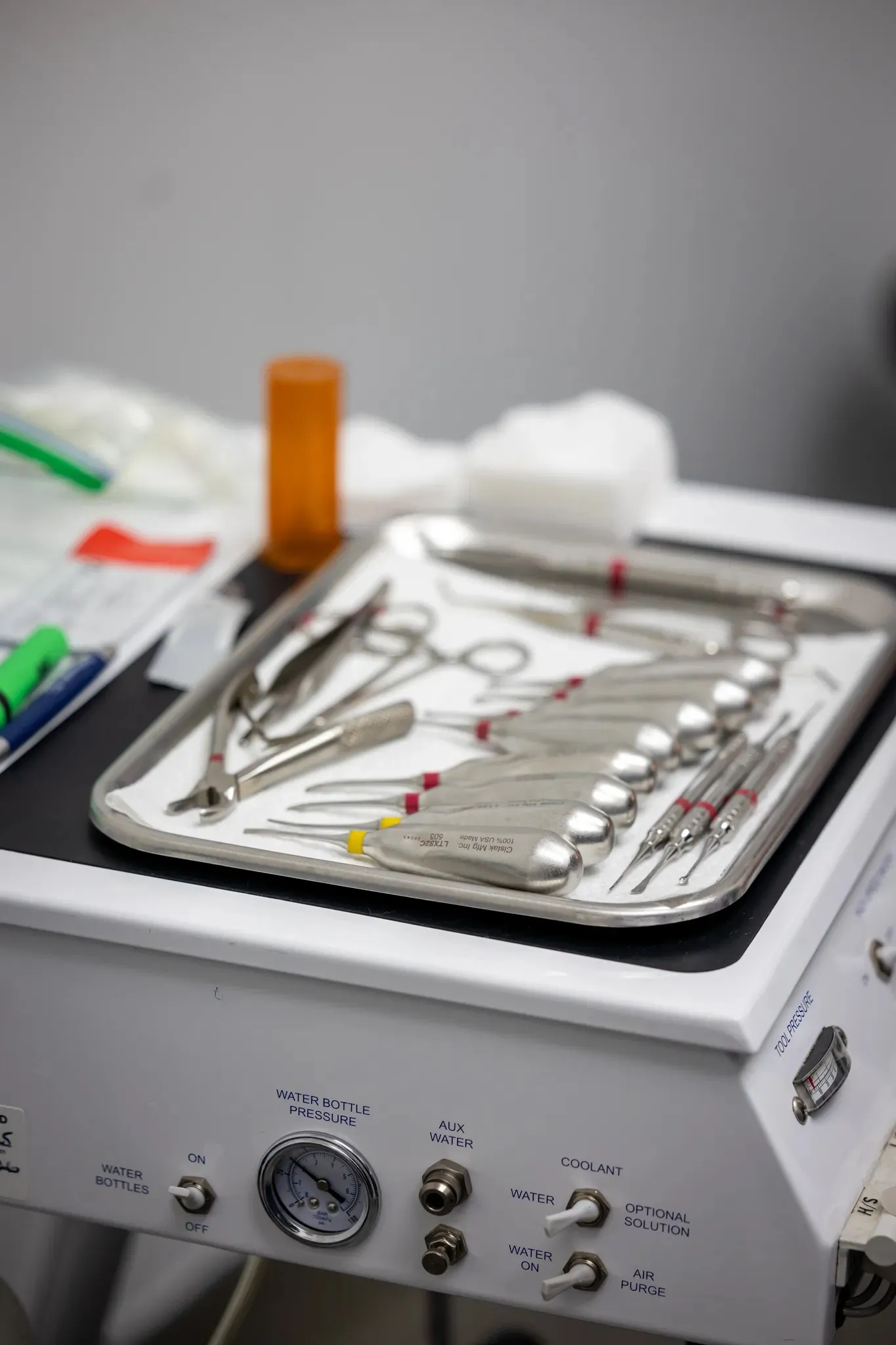 Tray of various dental instruments on a dental machine with pressure gauges and control switches.
