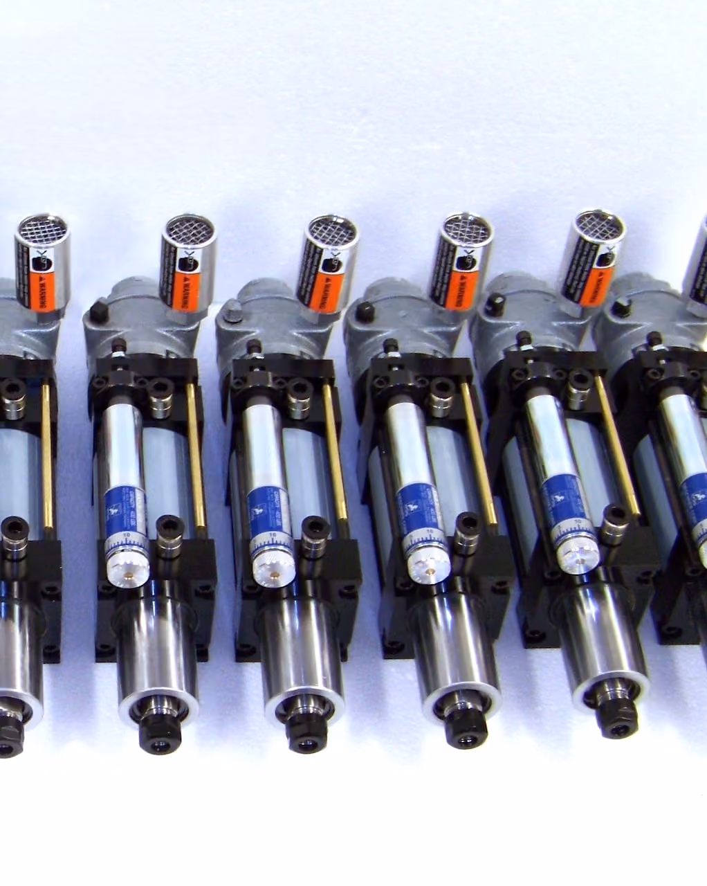 Six identical industrial pneumatic cylinders with pressure gauges and metal housings arranged in a row.
