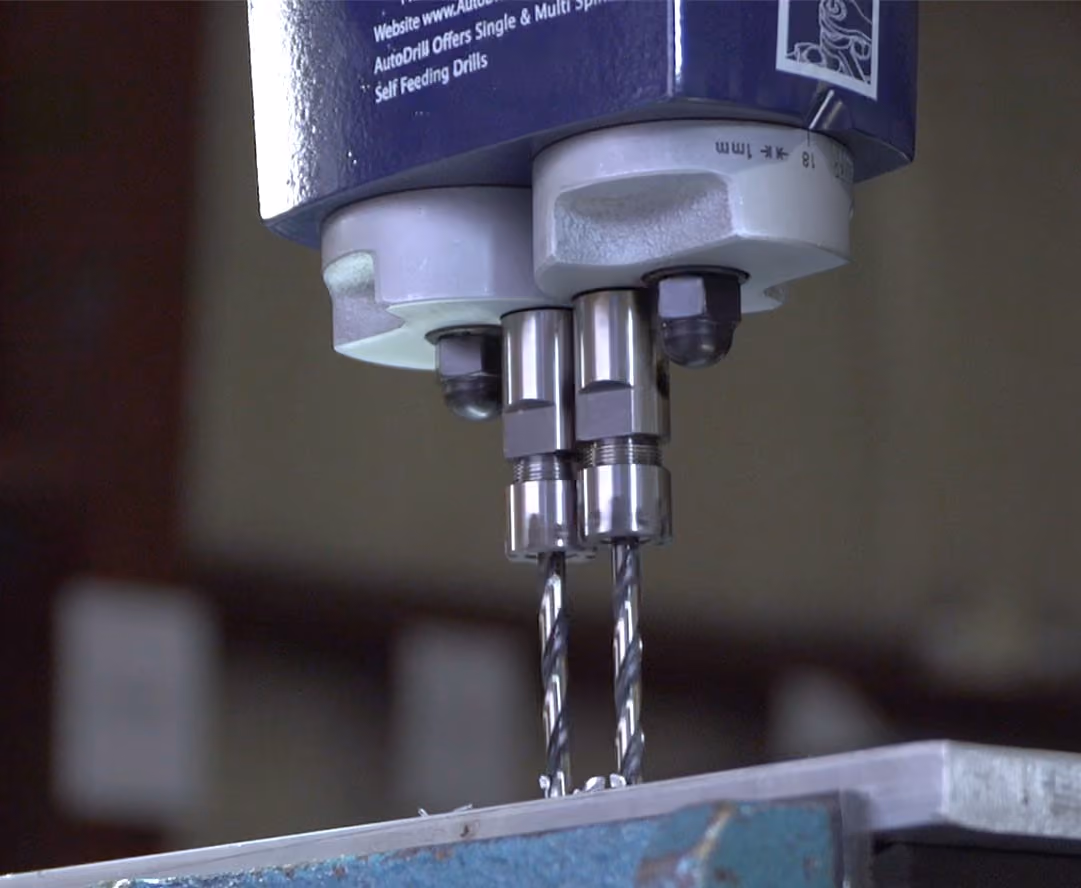 Close-up of a dual drill machine drilling into a metal surface with metal shavings around.