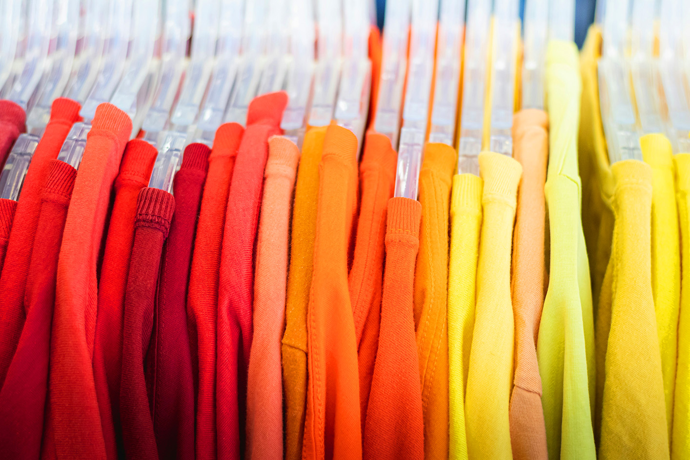 Clothes on hangers under bright lighting under LightLogics’ intelligent LED technology, highlighting vibrant red, yellow, and orange garments. 