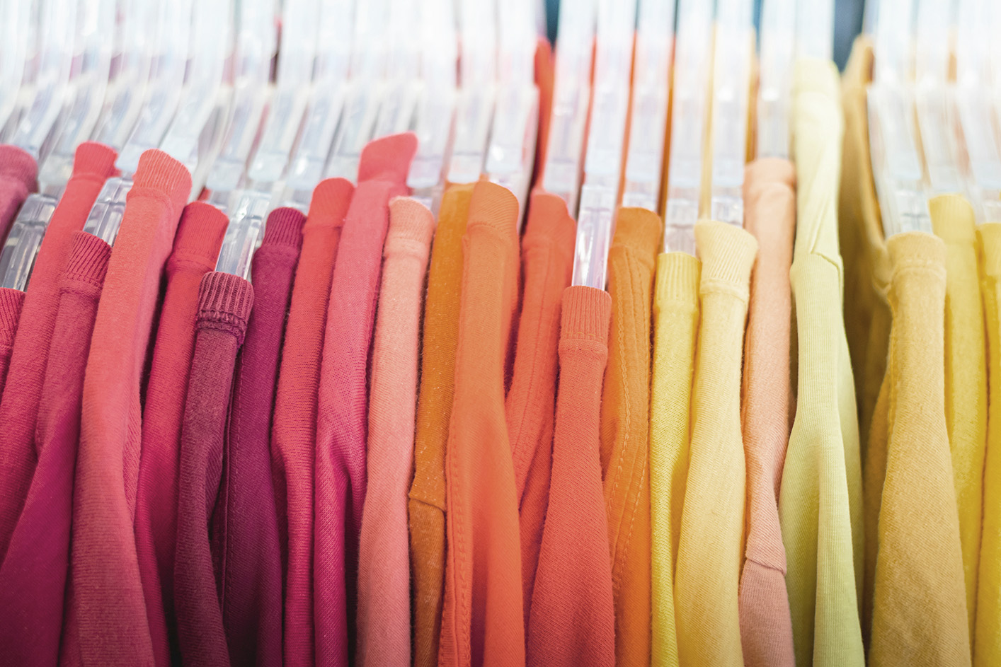 Clothes on hangers under poor lighting, featured faded and discoloured red, orange and yellow garments.