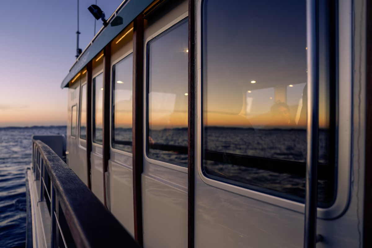 Side view of a boat with windows reflecting a sunset over calm water.