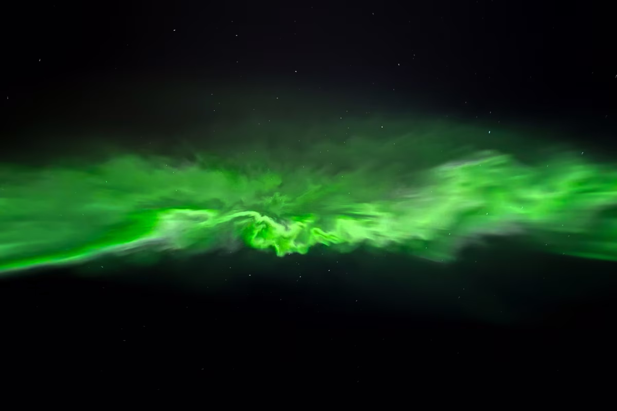 Green aurora borealis light streaks glowing against a dark night sky with stars.