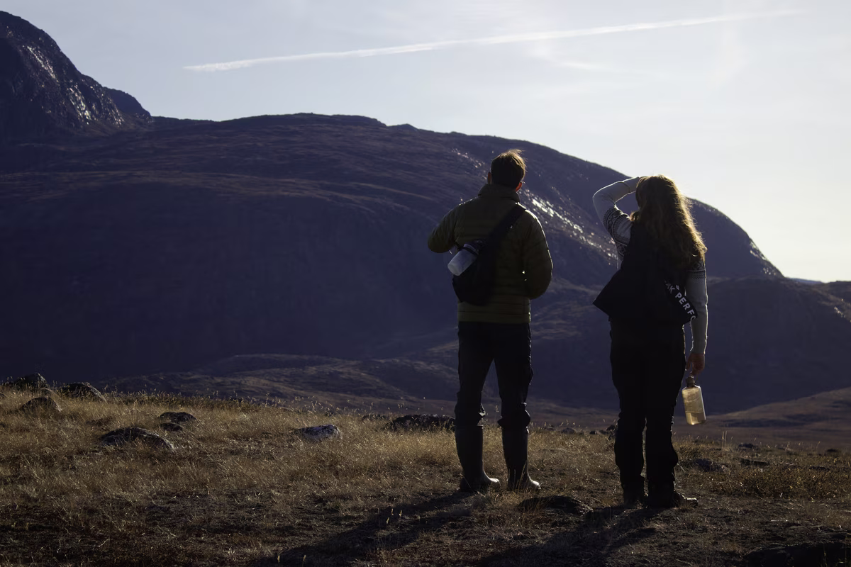 Two hikers standing on grassy land looking at distant mountains under a clear sky.