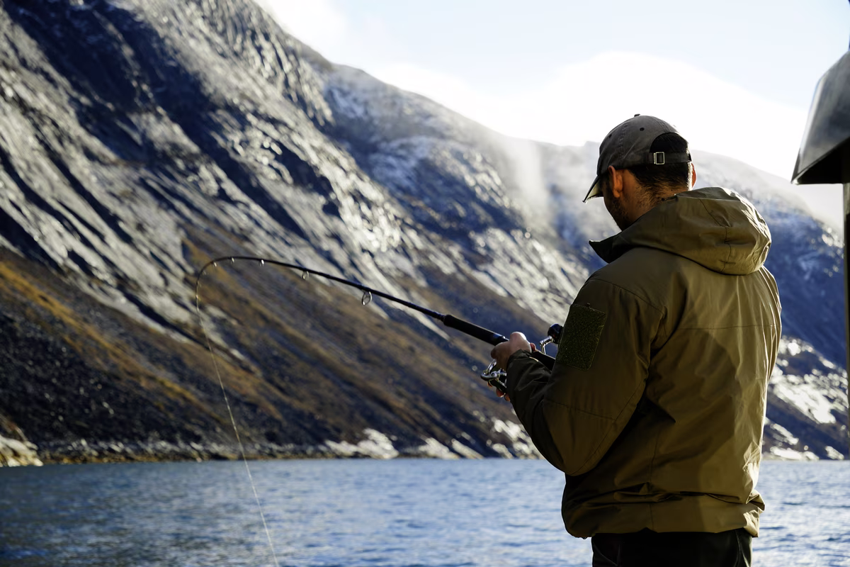 Man fishing on a lake with mountainous rocky cliffs in the background under daylight.