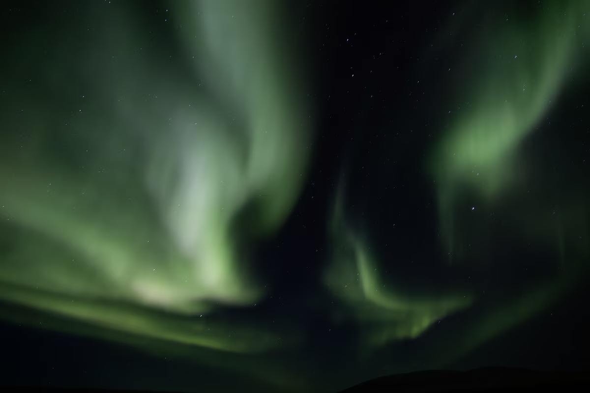 Green northern lights swirling against a dark starry night sky over a silhouette landscape.