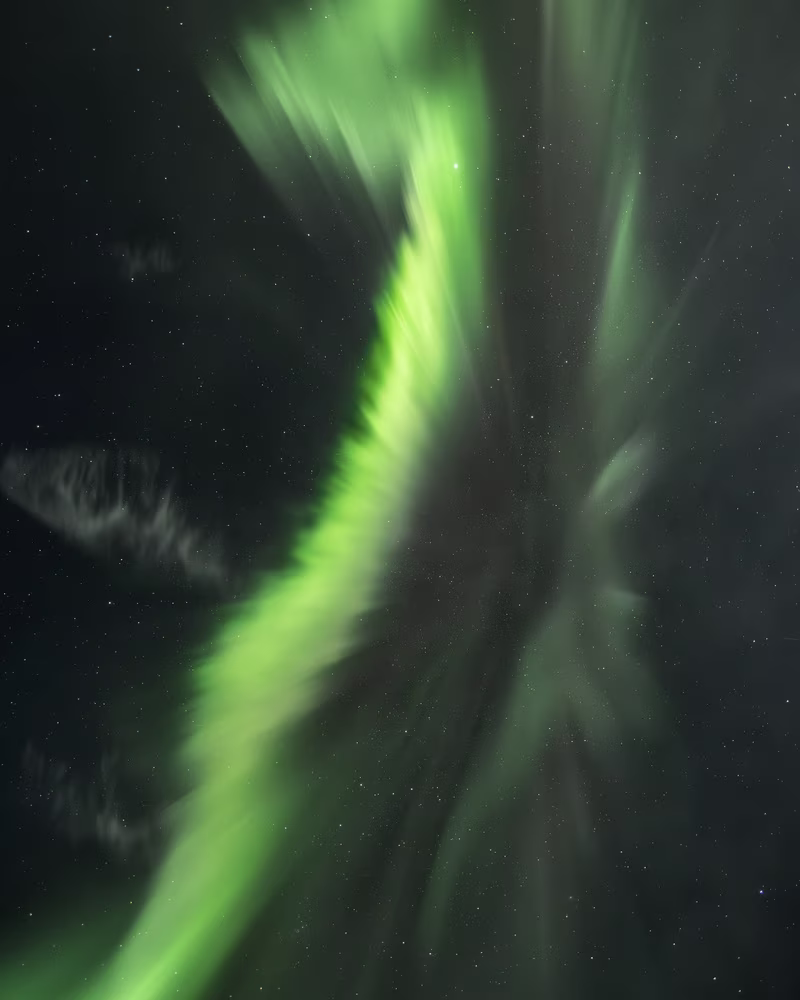 Green northern lights streak across a starry night sky.