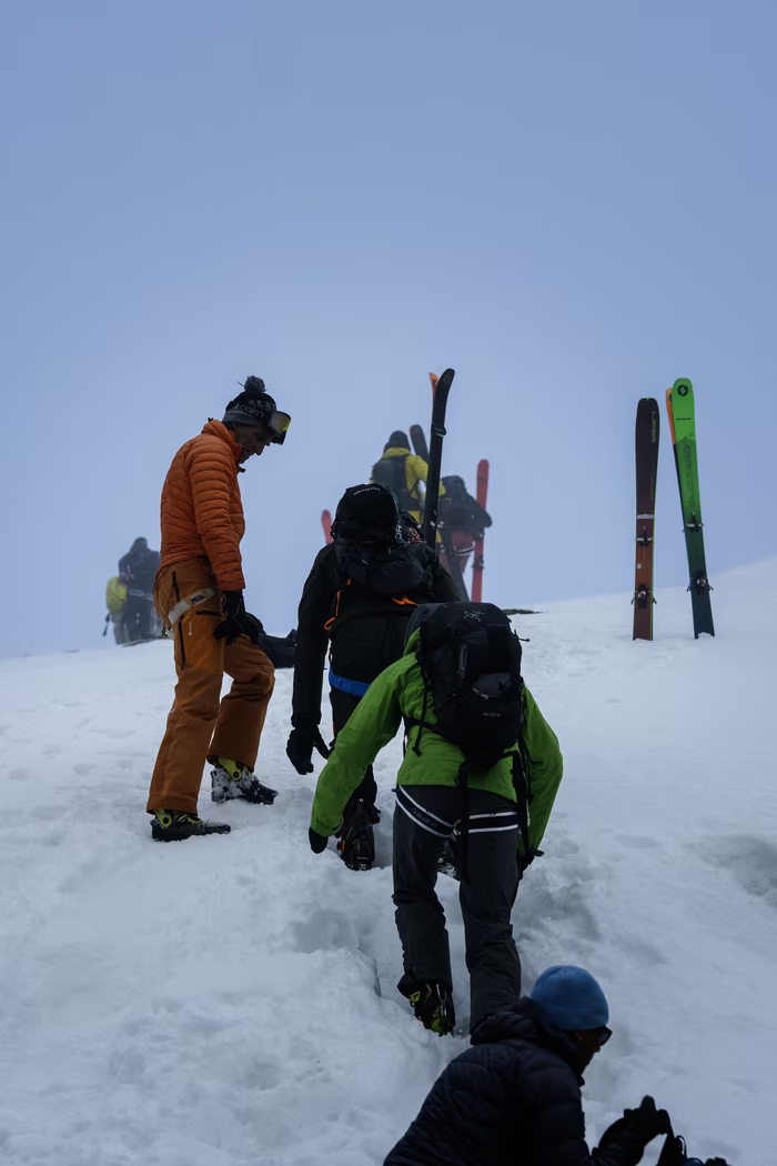 Group of skiers dressed in winter gear climbing a snowy slope on a foggy day.