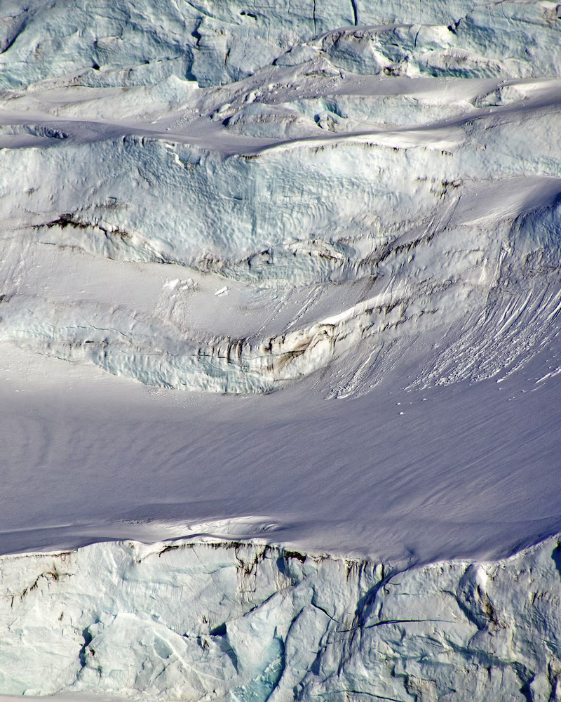 Aerial view of a snowy glacier with crevices and smooth ice surfaces.