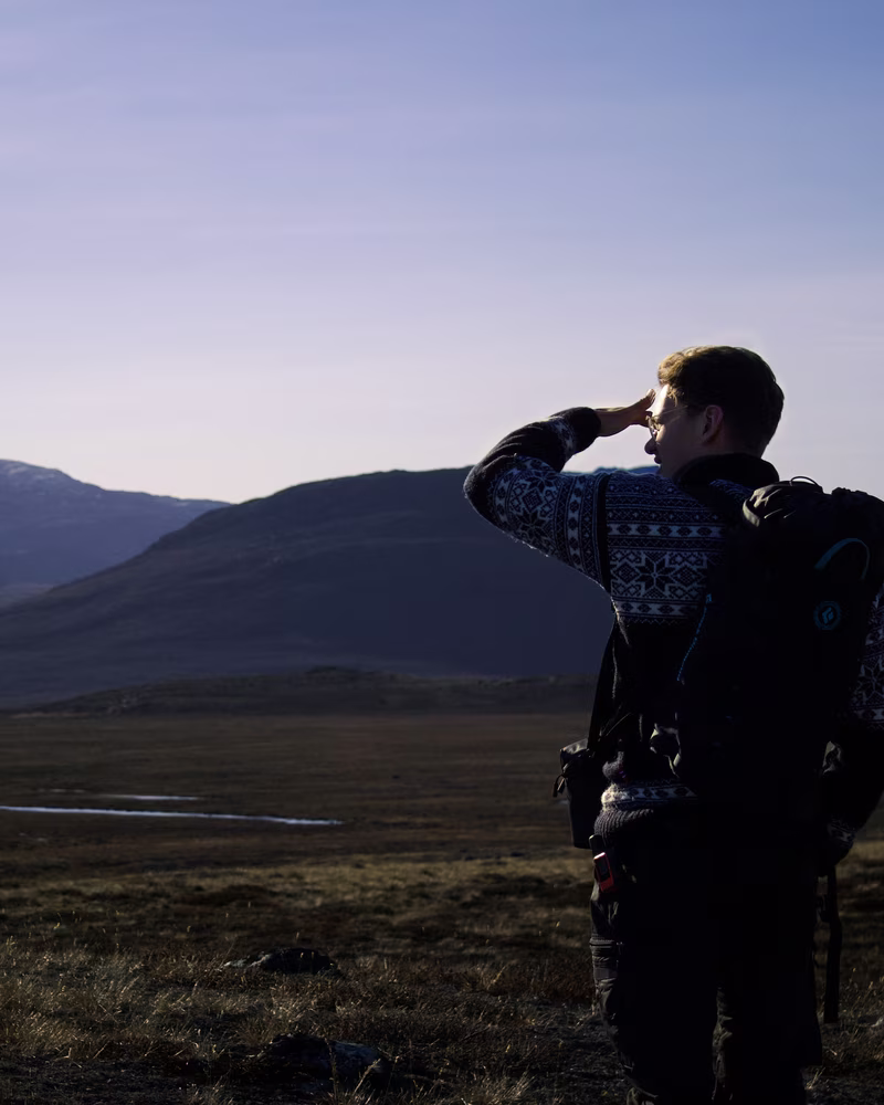 Person in patterned sweater with backpack gazing toward distant hills under a clear sky.