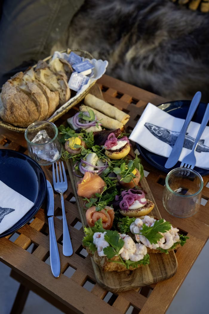 Wooden table set with plates, cutlery, glasses, bread basket, and a wooden board of assorted appetizers.
