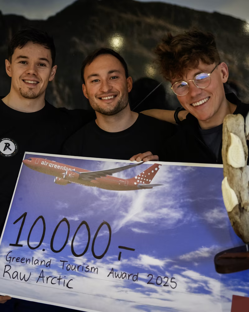 Three young men smiling and holding a large Greenland Tourism Award 2025 check for 10,000 DKK.