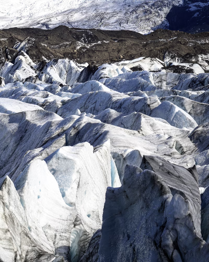 Jagged white and gray glacier ice formations with rocky terrain above them.