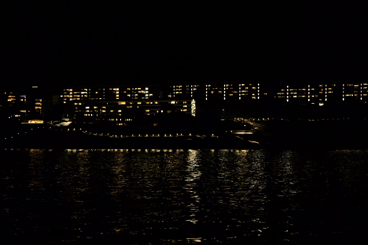 Night view of lit apartment windows reflecting on a calm body of water.