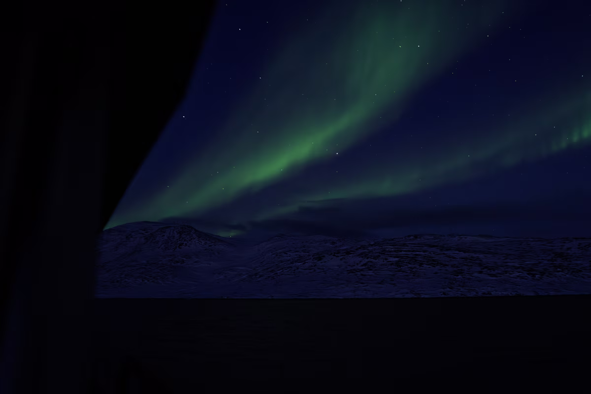 Northern lights glowing green over snowy mountains under a starry night sky.
