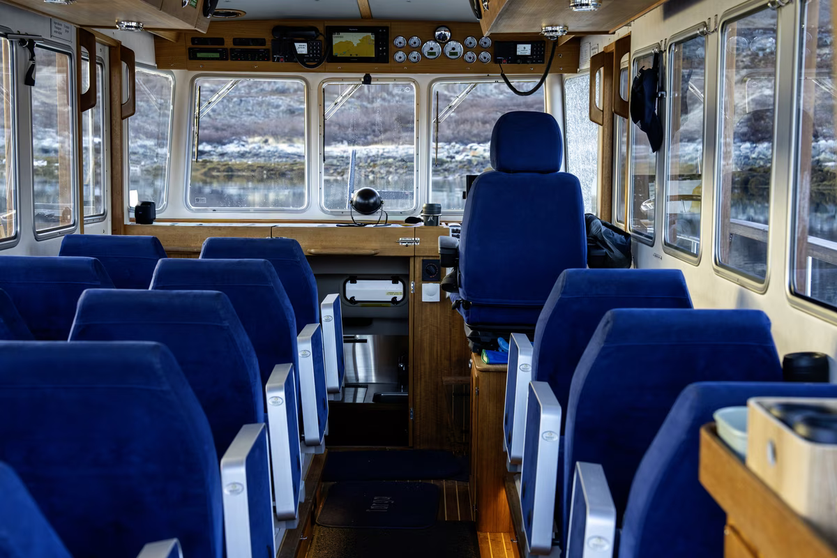 Interior of a boat cabin with blue seats facing forward and a captain's chair near control panels.
