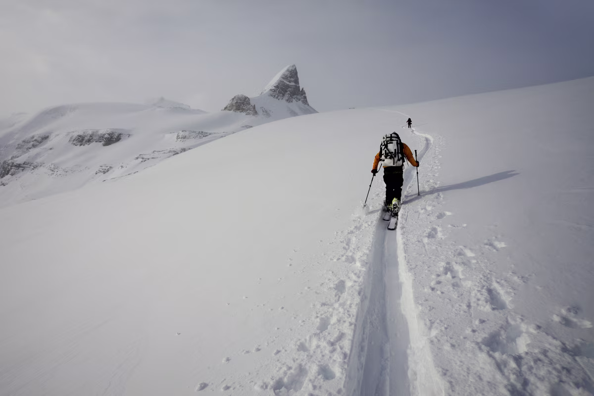 Skiers ascending a snowy mountain with a peaked rock formation in the background.