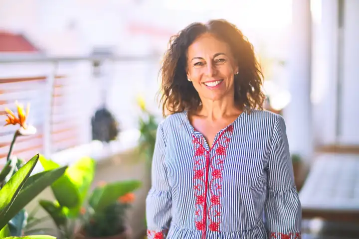 Smiling woman standing on a sunny balcony